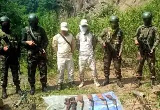 Armed security forces with weapons and equipment during a tactical operation in a rural setting.