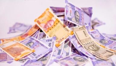 Indian currency notes, 100 and 2000 rupees, scattered on a white background.